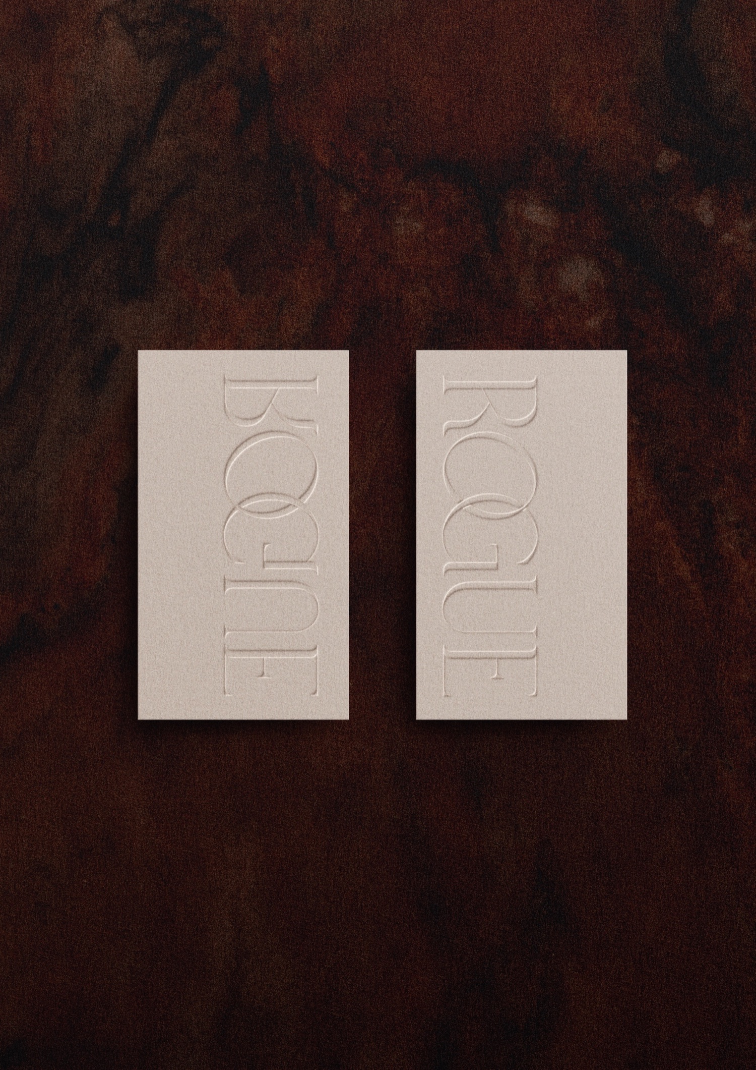 Two vertical Rogue embossed cards on a dark marble textured surface, showing the elegant curation of the print system